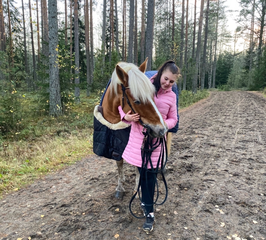 liinakkosuomenhevostamma syksyllä hiekkatiellä nuoren tummatukkaisen naisen kanssa