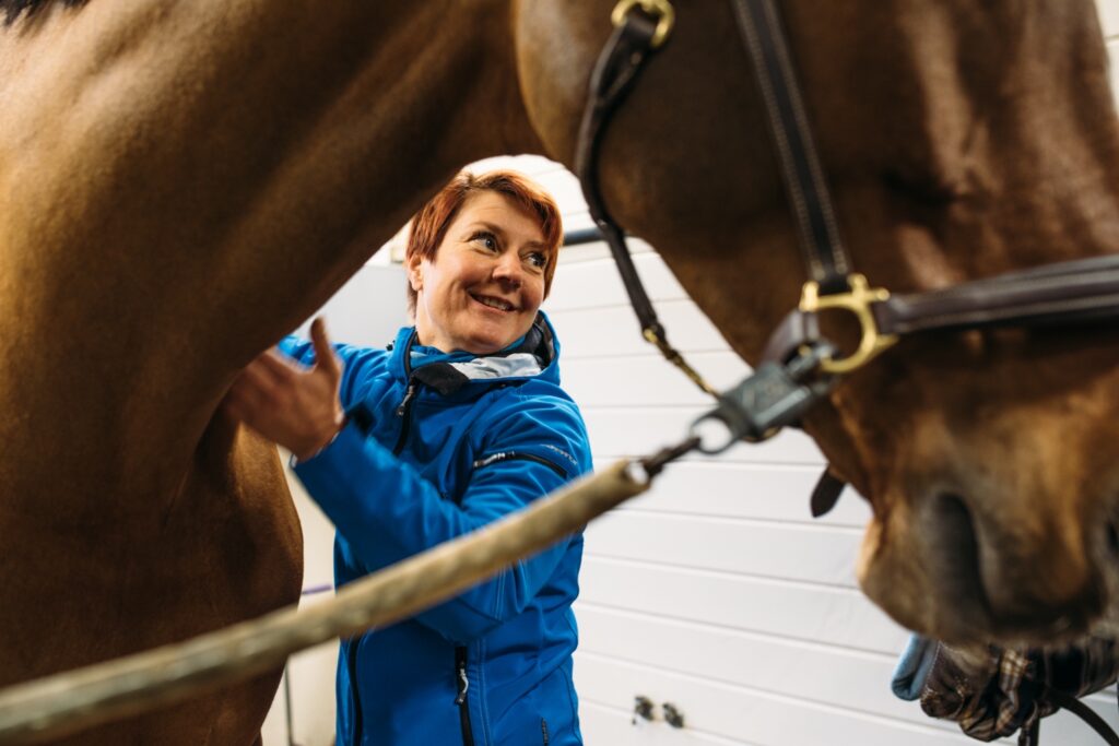 iloisesti hymyilevä nainen käsittelee hevosen lihaksia