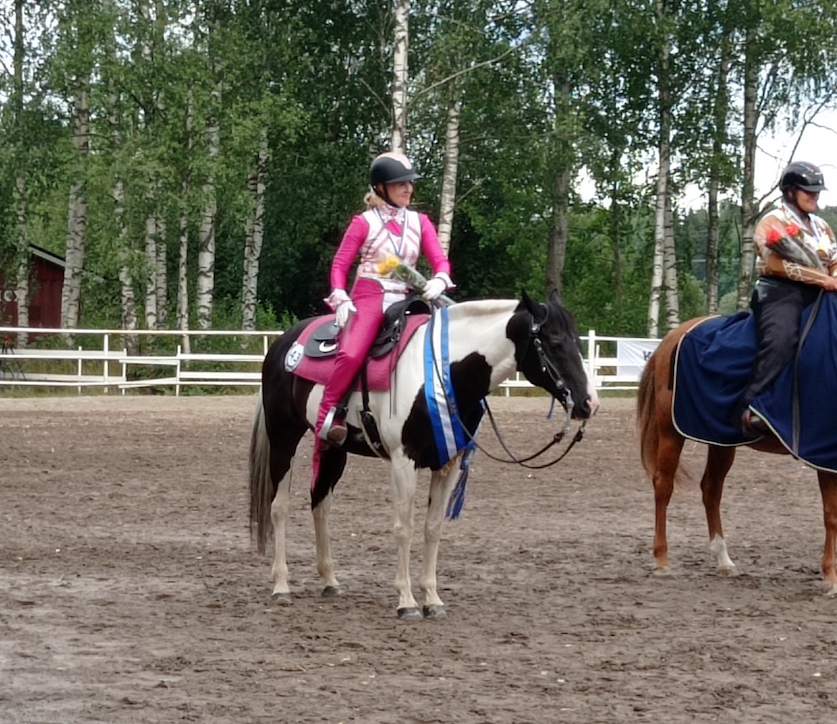 pinkkiin ja valkoiseen pukeutunut lännenratsastaja mustavalkokirjavan hevosen kanssa palkintojenjaossa